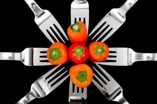 Still-life of Colorful peppers and shiny silver forks isolated on a black background 