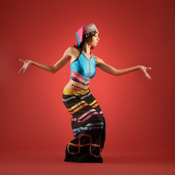 Mysterious China minority nationality girl dancing against red background.