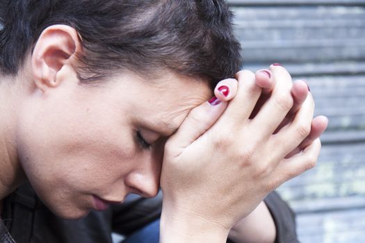 young woman in pain, his face pressed against his hands, his head bent down