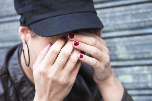 sad young woman wearing a cap, his face hidden in her hands