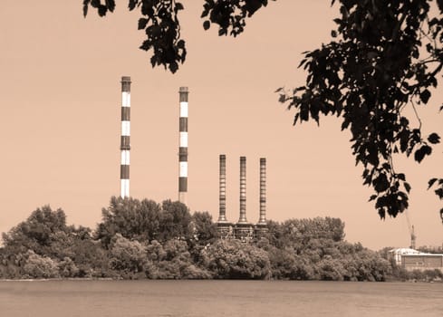 factory by Danube river, several chimneys behind trees in sepia tones