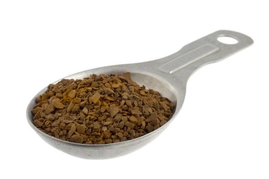 granules of instant coffee on old aluminum measuring tablespoon isoalted on white