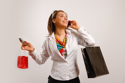 Modern looking young woman wearing white jacket talking on the phone and holding shopping bags