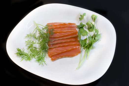 Salmon, fennel and parsley on a plate, a photo close up on a black background.