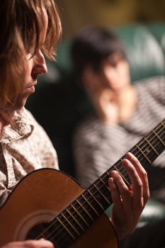 Young Musician Plays His Acoustic Guitar as Friend in the Background Listens.