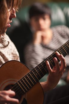 Young Musician Plays His Acoustic Guitar as Friend in the Background Listens.
