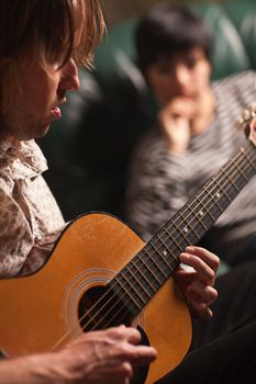 Young Musician Plays His Acoustic Guitar as Friend in the Background Listens.