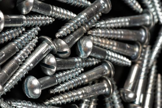 A heap of metal screws on black background