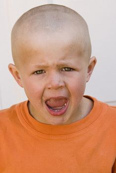 young frustrated boy with short hair, wearing orange shirt is screaming