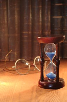 Vintage hourglass on background with old spectacles and books