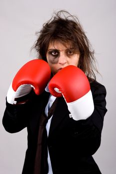 businesswoman wearing boxing gloves with bruised eye. grey background.