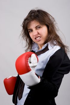 businesswoman wearing boxing gloves with confident attitude. grey background.