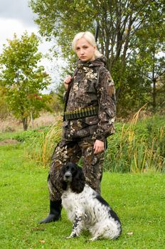 Blonde in camouflage with a gun and hunting dog.