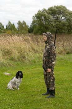 Blonde in camouflage with a gun and russian hunting spaniel.