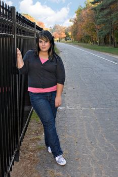 A young girl with highlighted hair posing by a fence on a nice autumn afternoon.