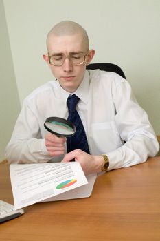 The boss with a magnifier in a hand on a workplace