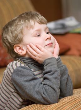 Cute little boy supporting his head with hands and looking at something