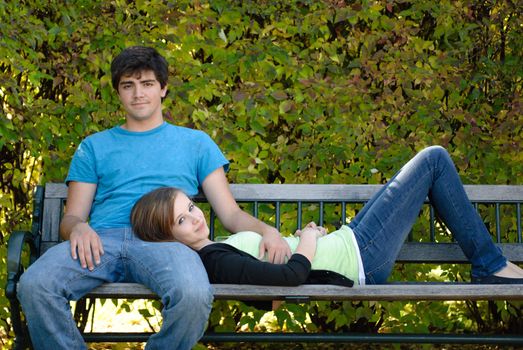 A young teenage girl is lying on a bench with her head on her boyfriend's lap.