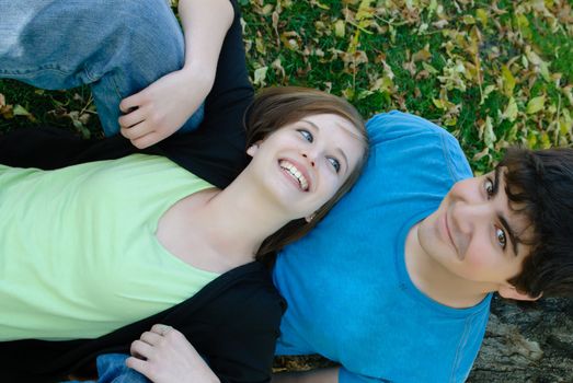 An top-down view of a teen couple lying on some leaves relaxing.