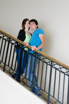 A teenage couple posing on a staircase smiling.