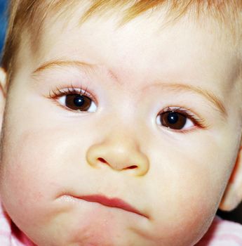 A young child is looking into the camera and sucking their lip.