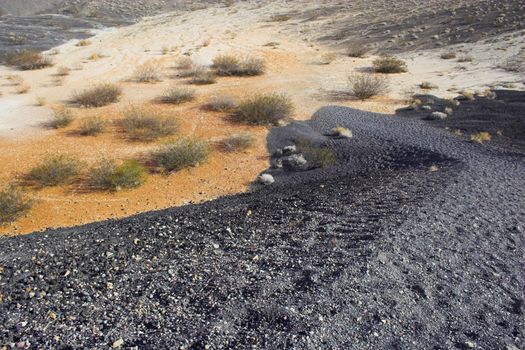 Fragment of black lava and ornage clay and salt mineral deposits in geological formations in Ubehebe Volcano, Death Valley National Park