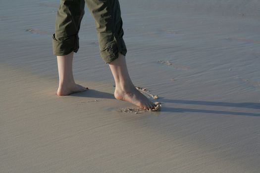 A woman dips her toes into the sand on the beach in the tide.