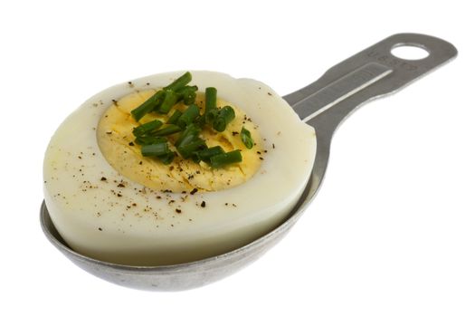 half of hard-boil egg with green chives and black pepper on old measuring tablespoon isolated on white
