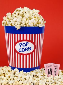 A popcorn bucket over a red background. Movie stubs sitting over the popcorn.