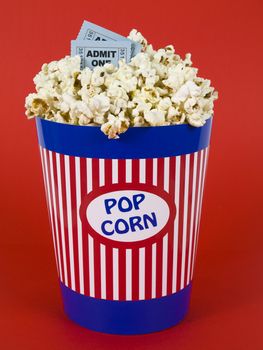 A popcorn bucket over a red background. Movie stubs sitting over the popcorn.