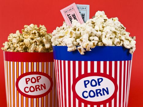 Two popcorn buckets over a red background. Movie stubs sitting over the popcorn.