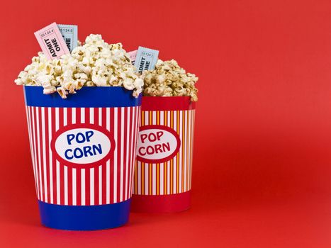 Two popcorn buckets over a red background. Movie stubs sitting over the popcorn.