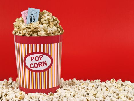 A popcorn bucket over a red background. Movie stubs sitting over the popcorn.