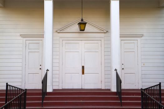 Red stairs leading to four white church doors wth black railing