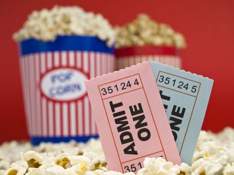 Two popcorn buckets over a red background. Movie stubs sitting over the popcorn.