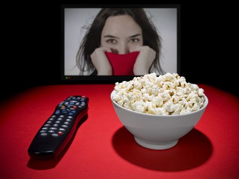 A popcorn bowl and a remote control. A wide TV screen as a background.