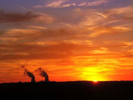 The sun sets over two giant cooling towers at a nuclear plant.