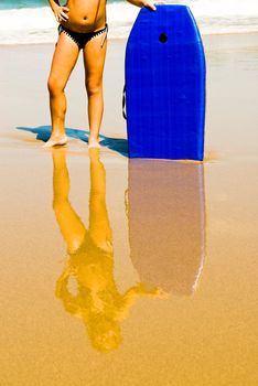 Young girl standing on the beach with reflection in the water on the sand