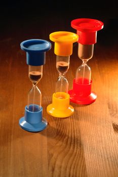 Three colored hourglasses standing on wooden background