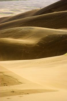 People small like aints walking far-away in dunes with sand being blown over by wind 