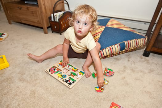 Cute little European toddler girl having fun with wooden puzzle.