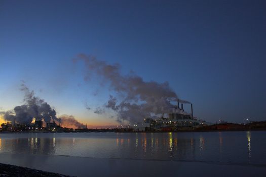 Factory over the river with smoke coming out of the chimneys