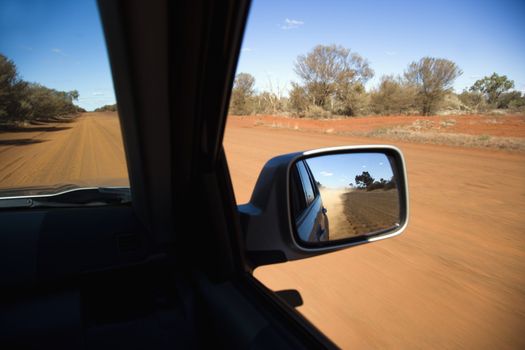 Vehicle on dirt road with rear view mirror reflection of rural Australia.