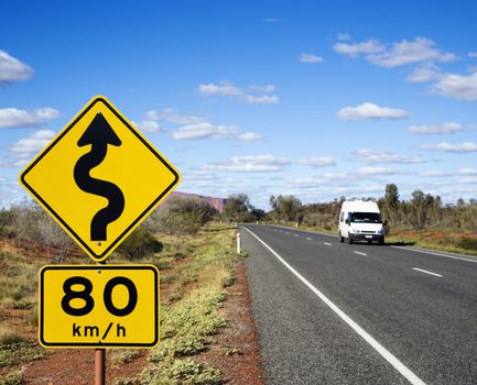 Van on asphalt two lane road in rural Australia with speed limit and curve ahead road sign.