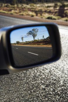 Reflection of rural Australian in rearview mirror of vehicle traveling down two lane asphalt road.