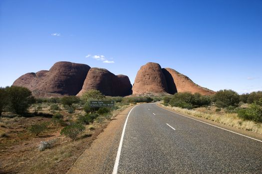 Two lane road in Uluru Kata Tjuta National Park, Australia with Mount Olga in the distance.
