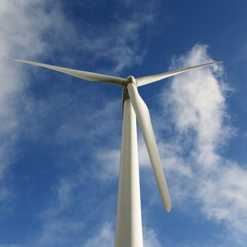 Low angle view of wind turbine against blue sky and clouds.