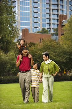 Family of four people walking in park smiling.