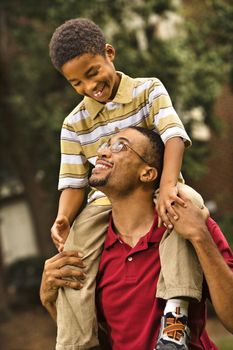 Father carrying his son on his shoulders smiling and looking at eachother.