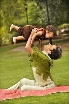 Woman holding toddler up in air and smiling in park.